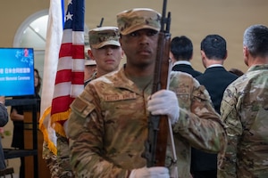 Airmen of the base honor guard hold a rifle and a flag while waiting to present the colors.
