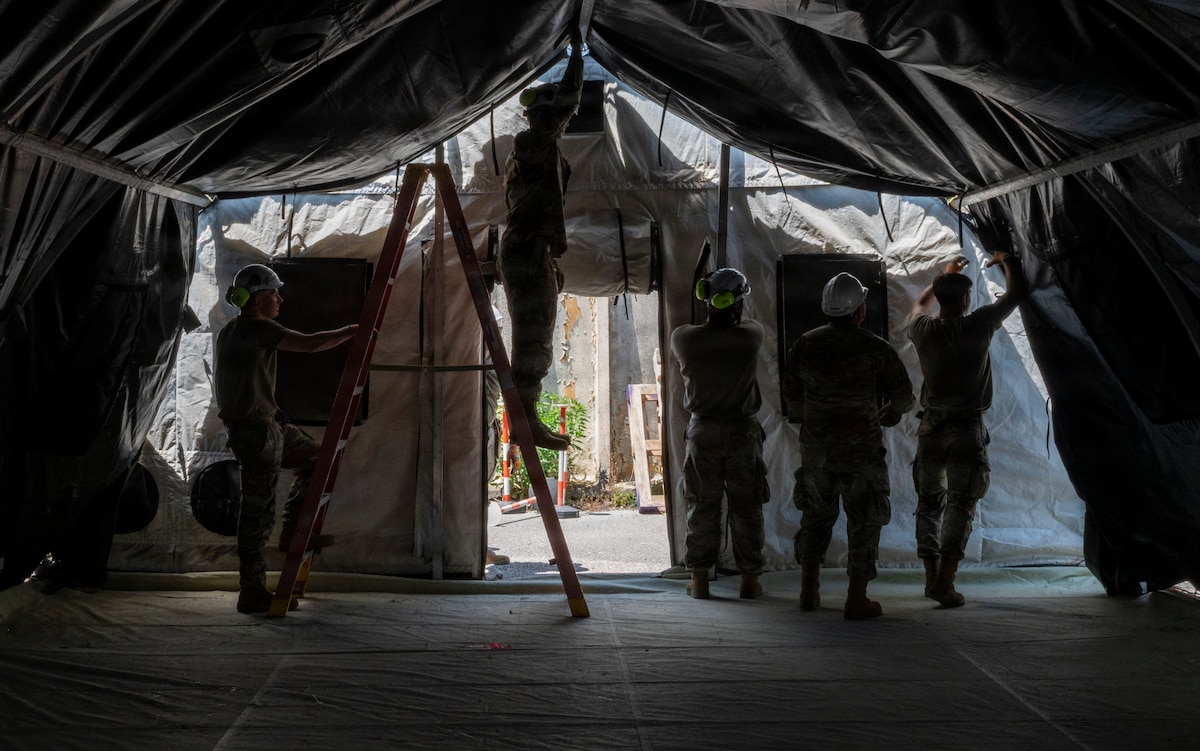 A group of men strap a canvas ceiling to a tent frame.