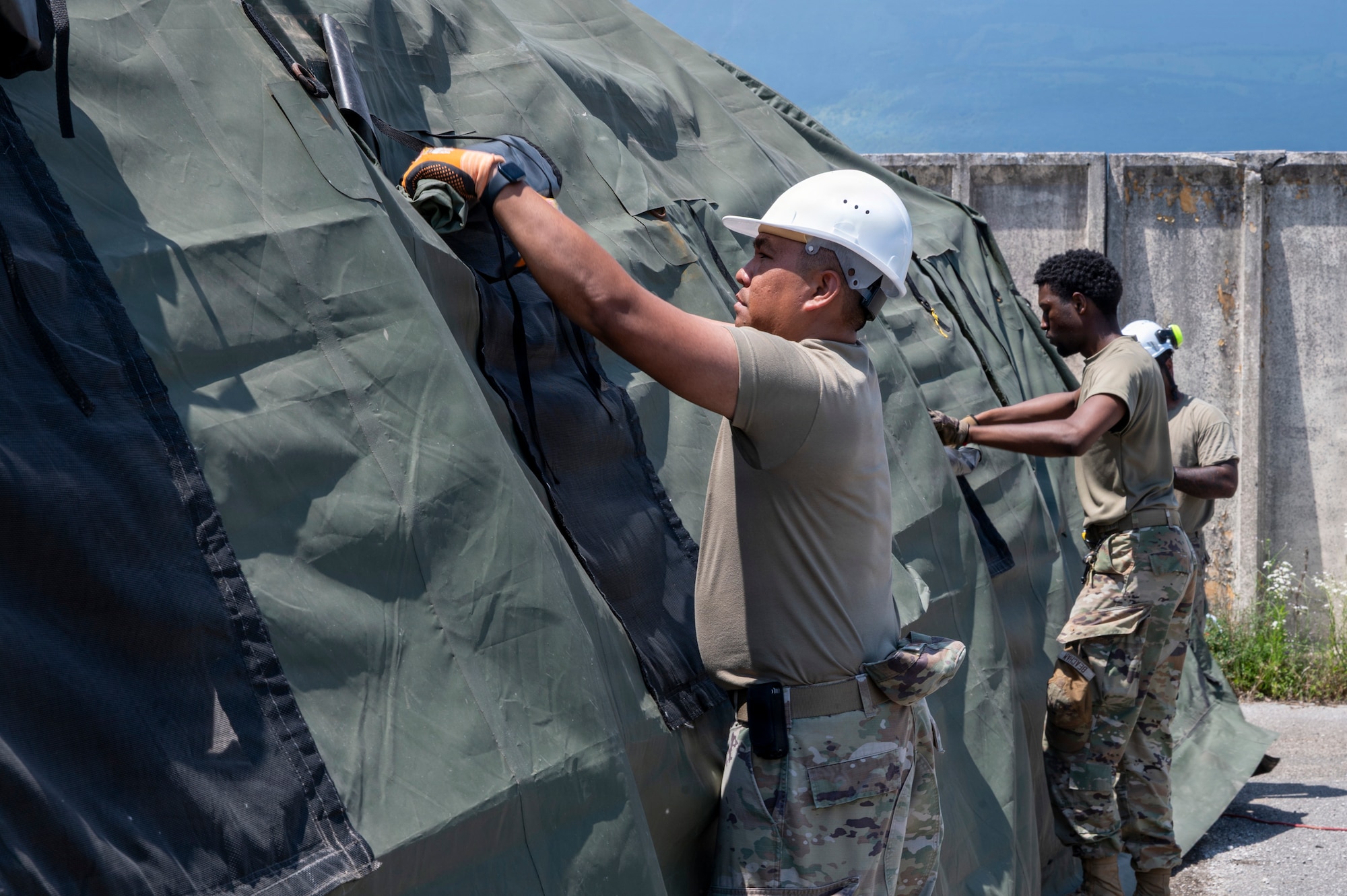 A man rolls up the canvas window covering on a small system shelter.