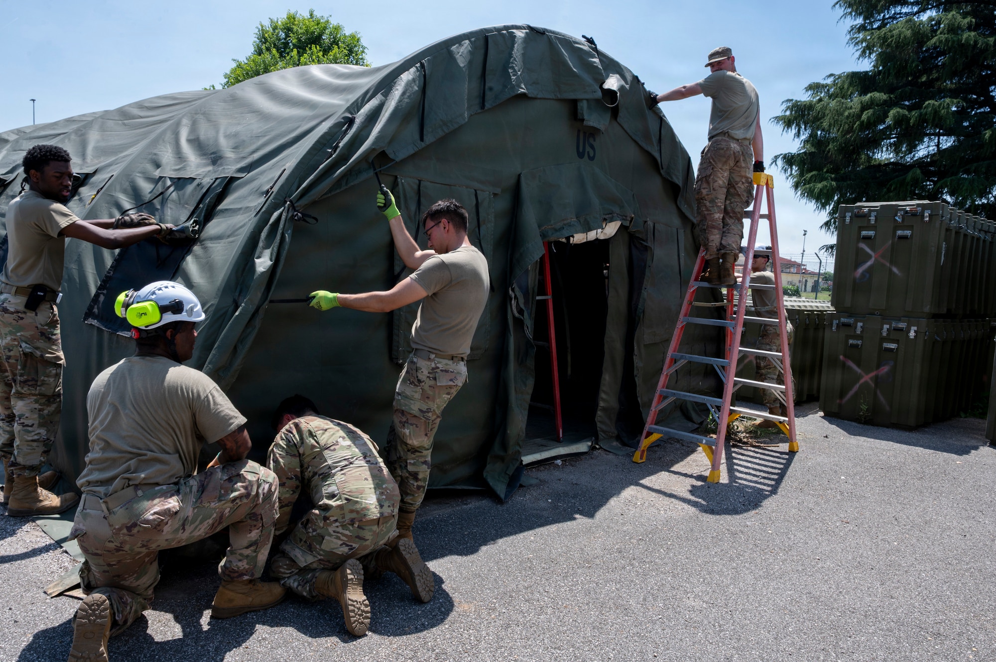 A group of men secure the canvas of a small system shelter.