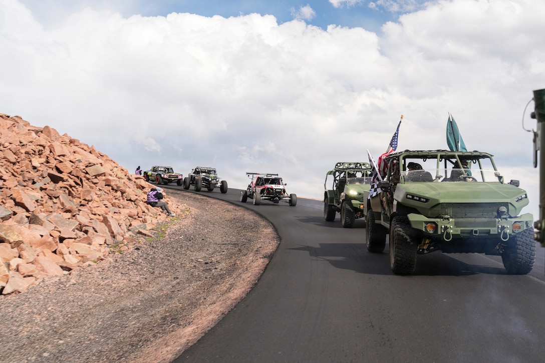 Five race vehicles turn down a rocky hill against a cloudy sky.