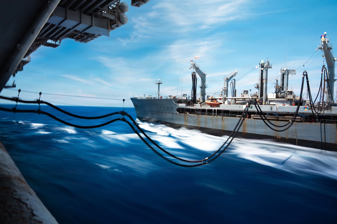A partially visible ship is connected by two black lines to another ship in a blurry ocean under a blue sky.