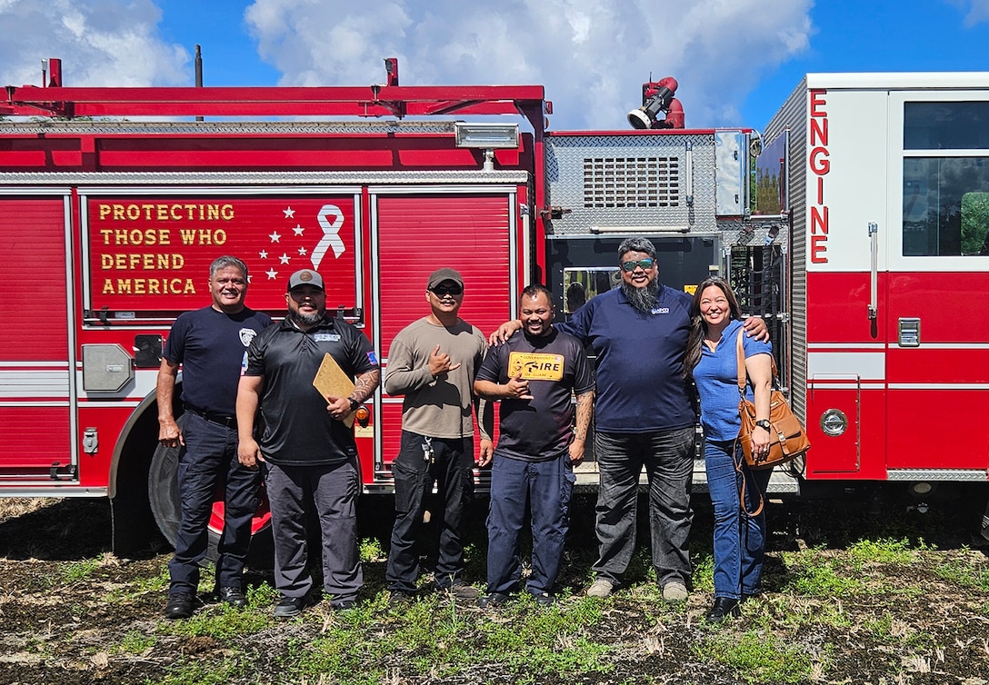 Six people pose in front of a firetruck.