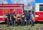 Six people pose in front of a firetruck.