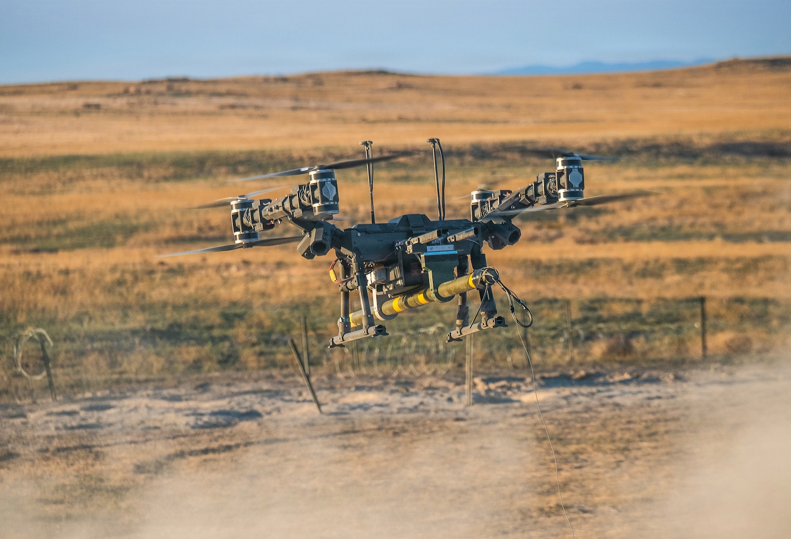A Lorica Technologies Inc. Mule 28 unmanned aerial system carries a live, primed M1A3 Bangalore torpedo toward a concertina wire obstacle moments before release June 22, 2026, on Range 22 at Orchard Combat Training Center, Idaho.
