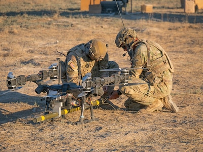 Sgt. 1st Class Raynaldo Villarreal, left, and 1st Sgt. Joshua Martin prime a live M1A3 Bangalore torpedo by connecting shock tube to the charge before a drone-delivered breach attempt against a concertina wire obstacle June 22, 2026, on Range 22 at Orchard Combat Training Center, Idaho.