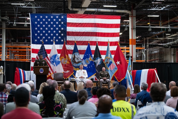 A man wearing a military uniform stands on stage behind a podium speaking into a microphone