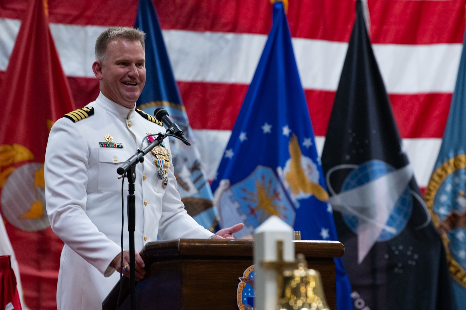 A man wearing a military uniform stands on stage behind a podium speaking into a microphone