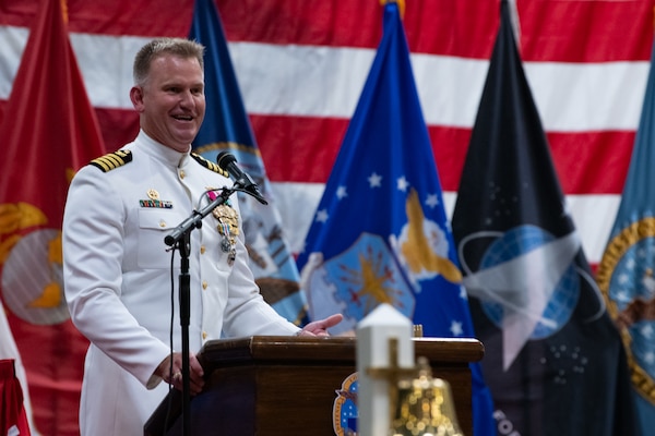 A man wearing a military uniform stands on stage behind a podium speaking into a microphone