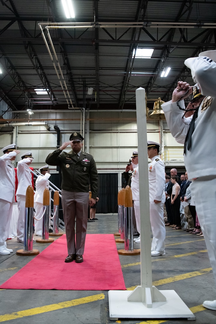 A man wearing a military uniform is saluted by other men as he walks down a red carpet.