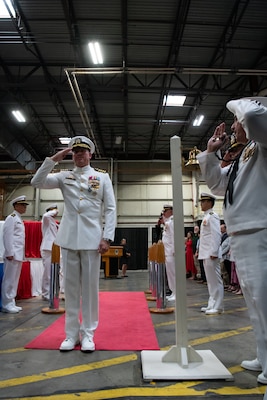 A man wearing a military uniform is saluted by other men as he walks down a red carpet.