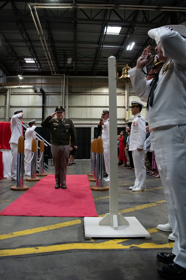 A man wearing a military uniform is saluted by other men as he walks down a red carpet.