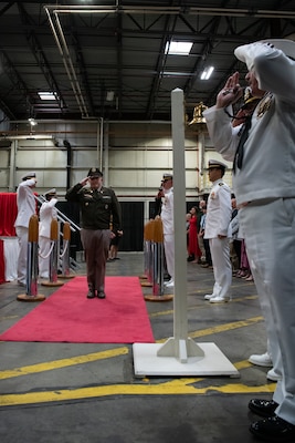 A man wearing a military uniform is saluted by other men as he walks down a red carpet.