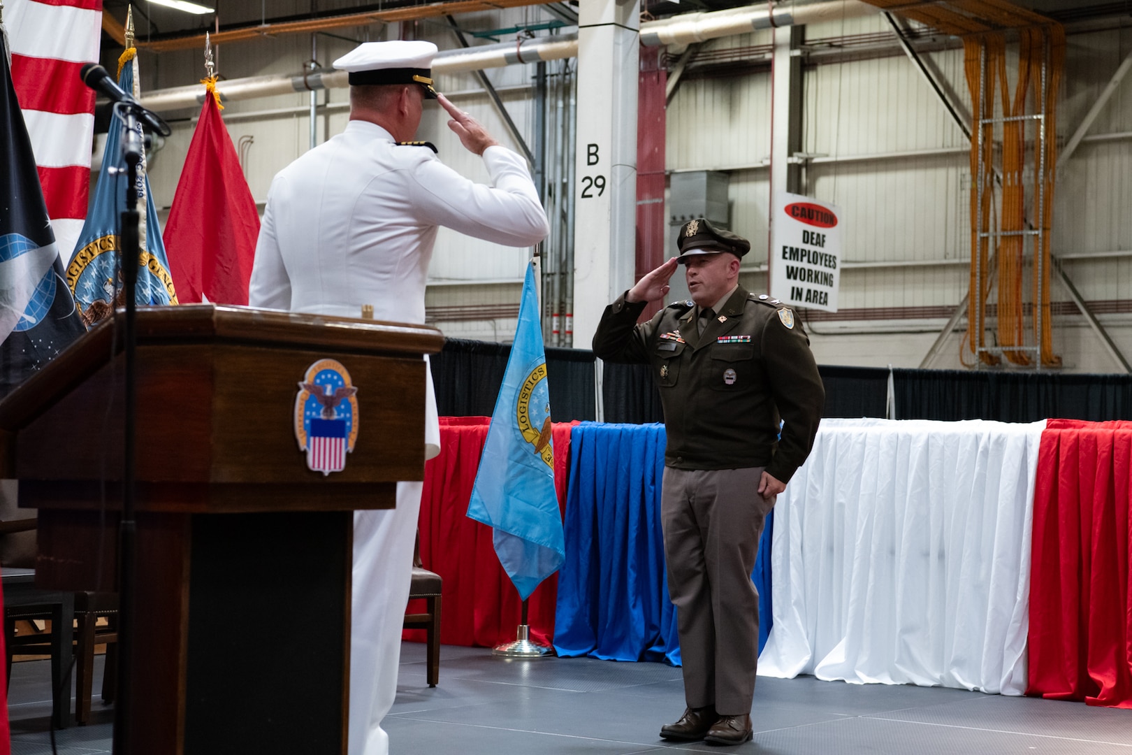Two men wearing military uniforms salute each other on stage