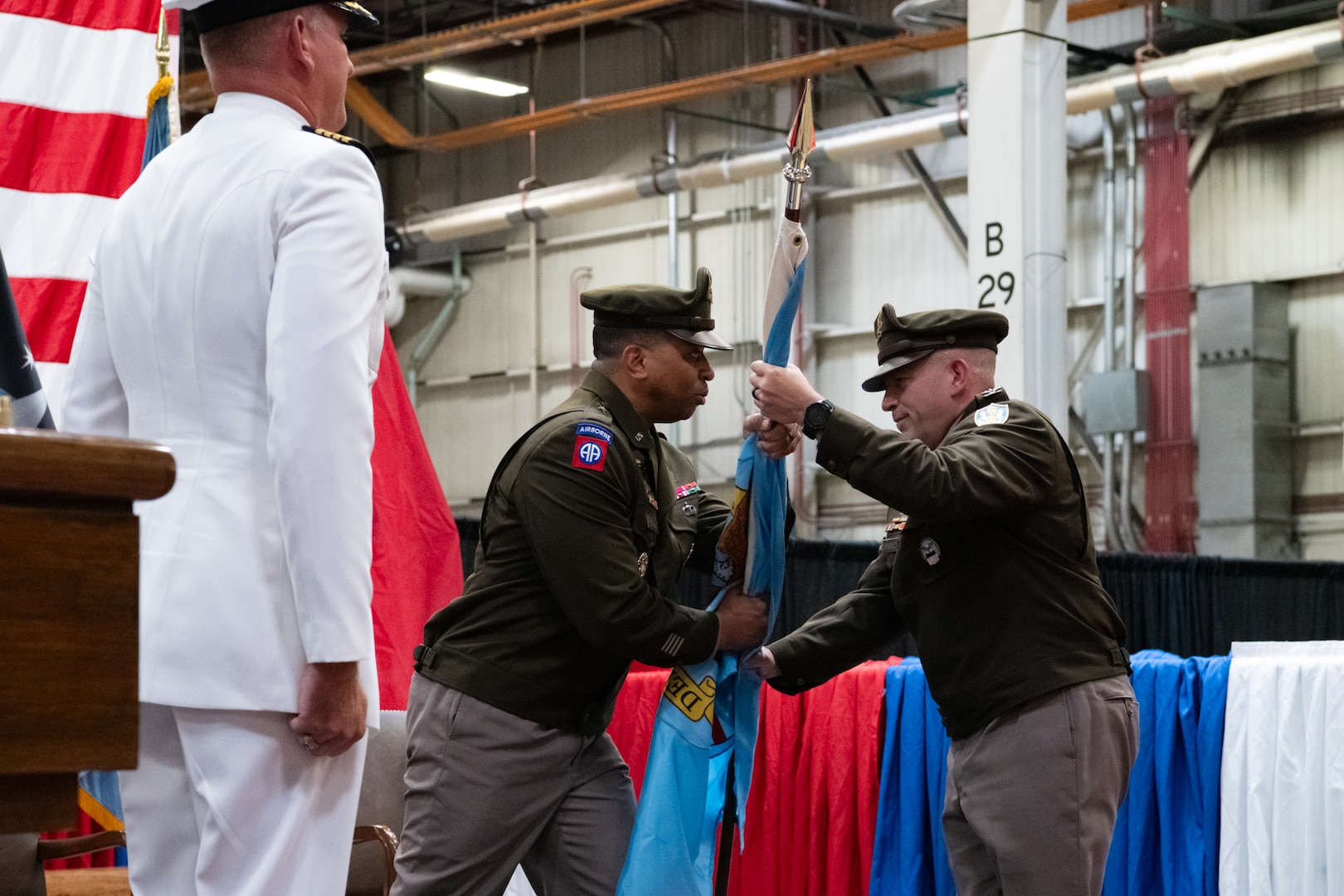 Two men wearing military uniforms pass a flag between them.