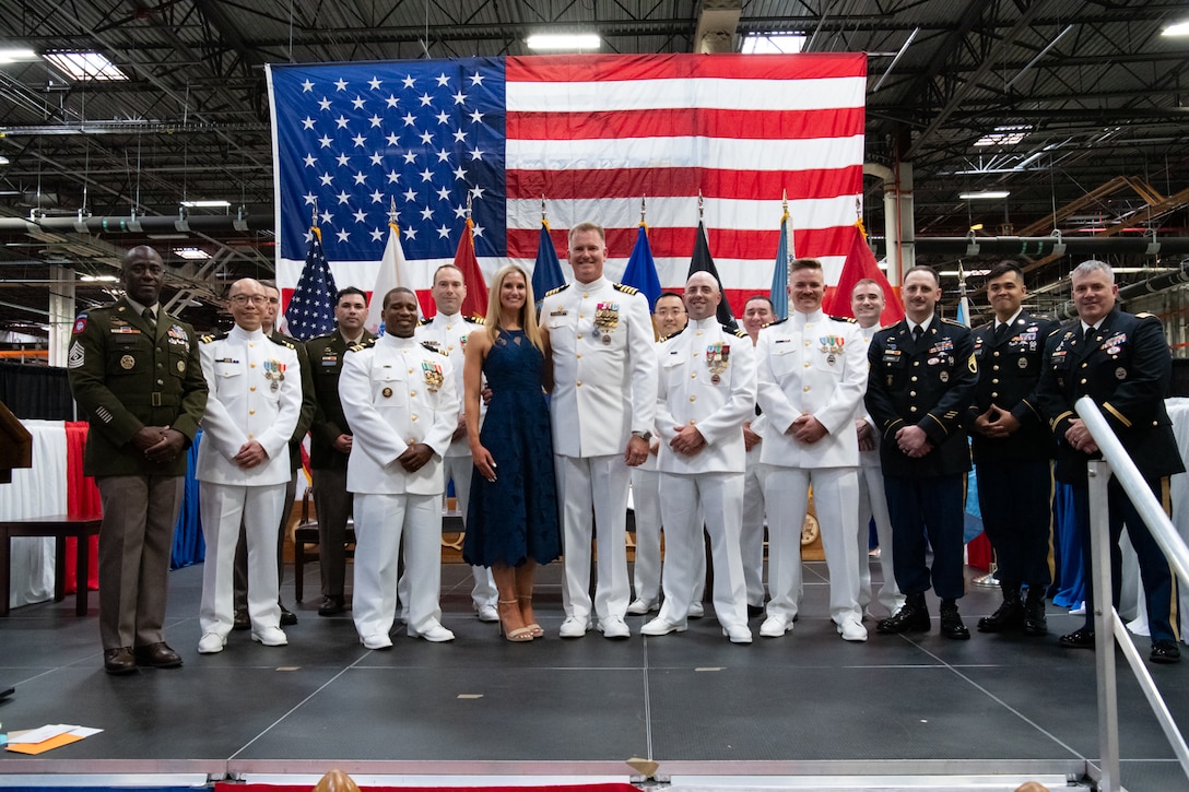 A group of people wearing military uniforms pose on stage for a group photo.