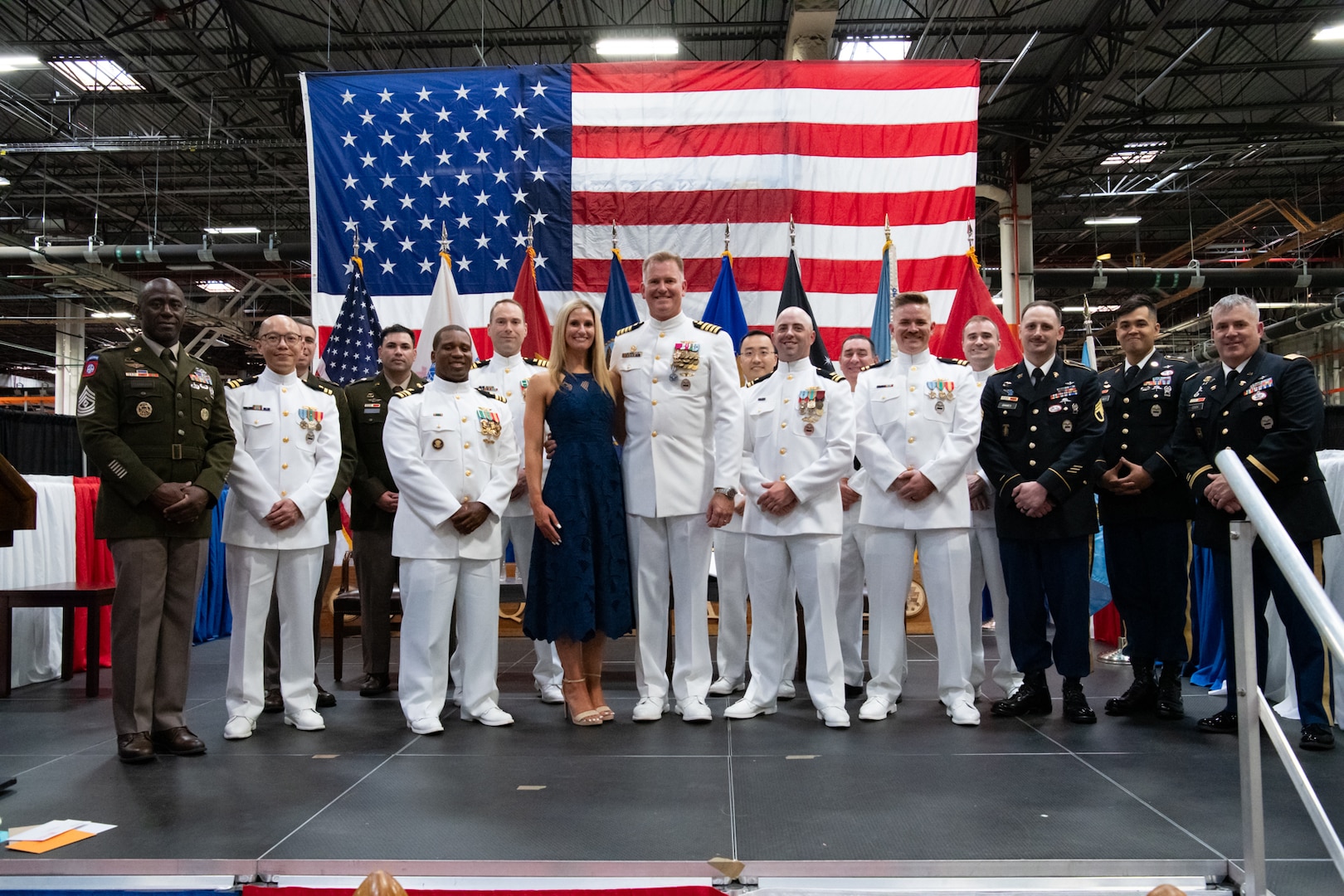 A group of people wearing military uniforms pose on stage for a group photo.