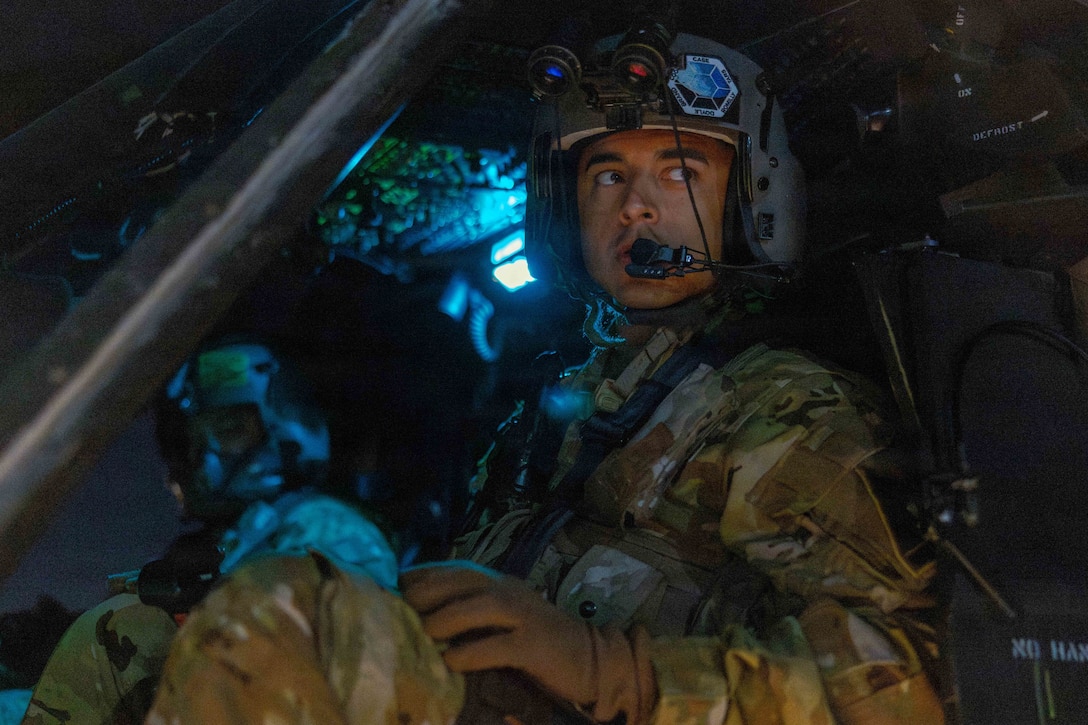 A military pilot looks to his left while sitting in a helicopter at night, with his copilot seated next to him.