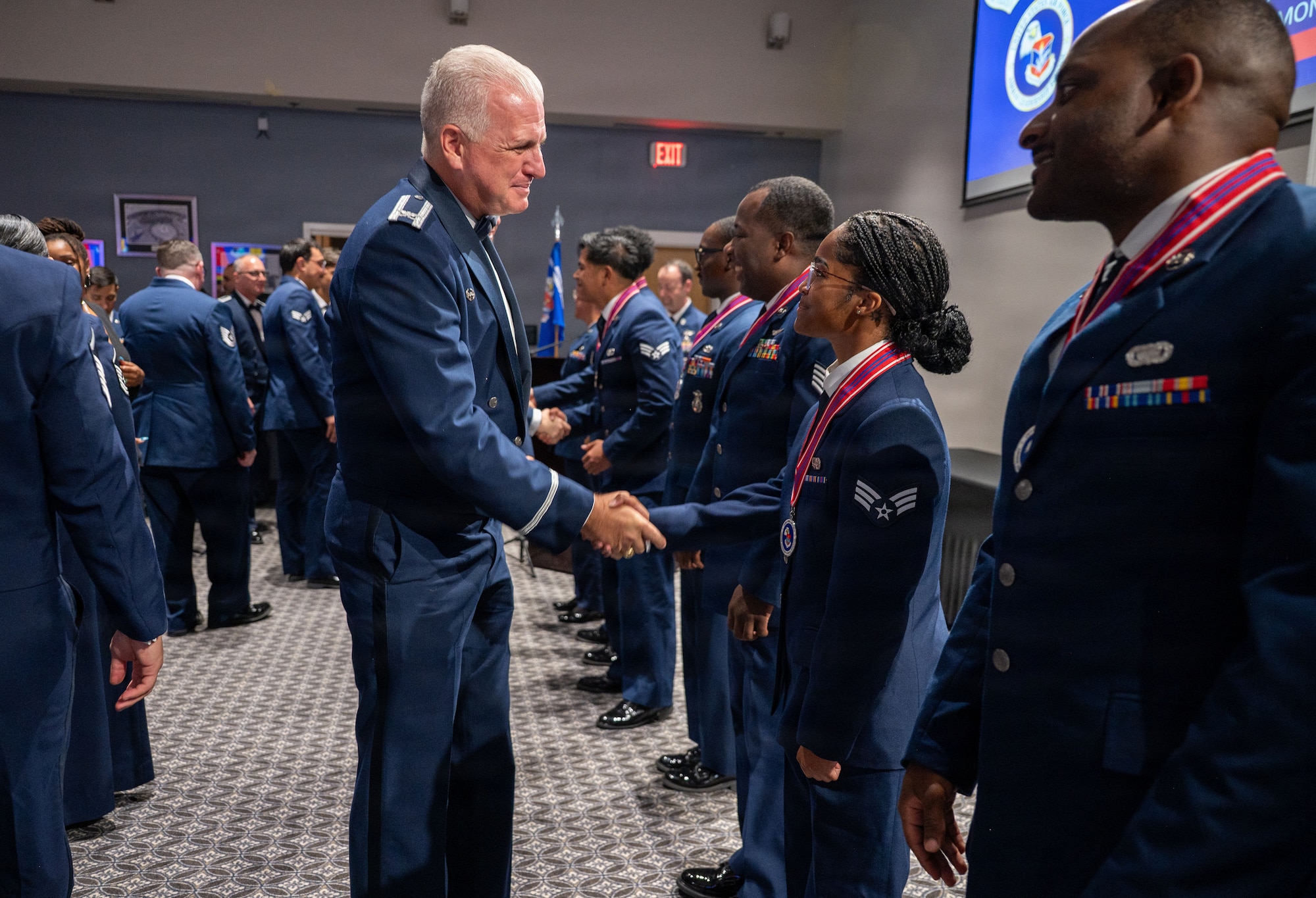 Two service members shake hands in front of a crowd of people