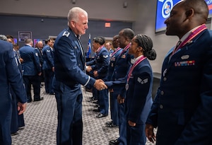 Two service members shake hands in front of a crowd of people