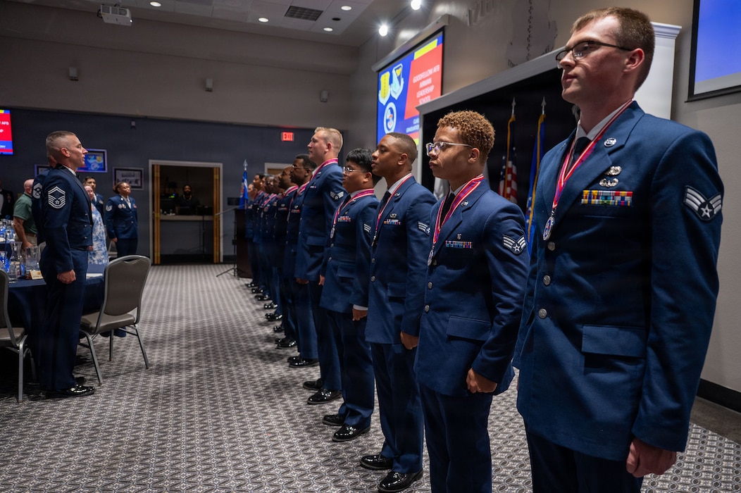 A line of 12 service members stand at attention in front of a crowd