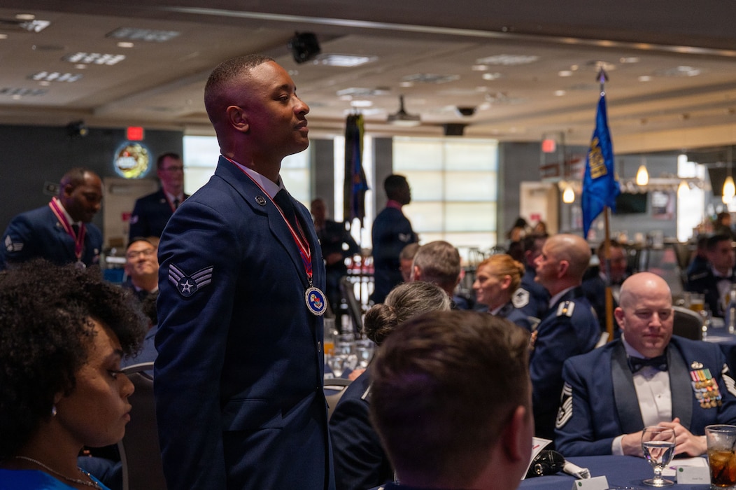 A service member with a medallion stand at a round table with others sitting