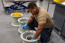 A U.S. Air Force maintainer wearing blue protective gloves kneels on the shop floor while assembling C-17 Globemaster III wheel rim components in a maintenance shop.