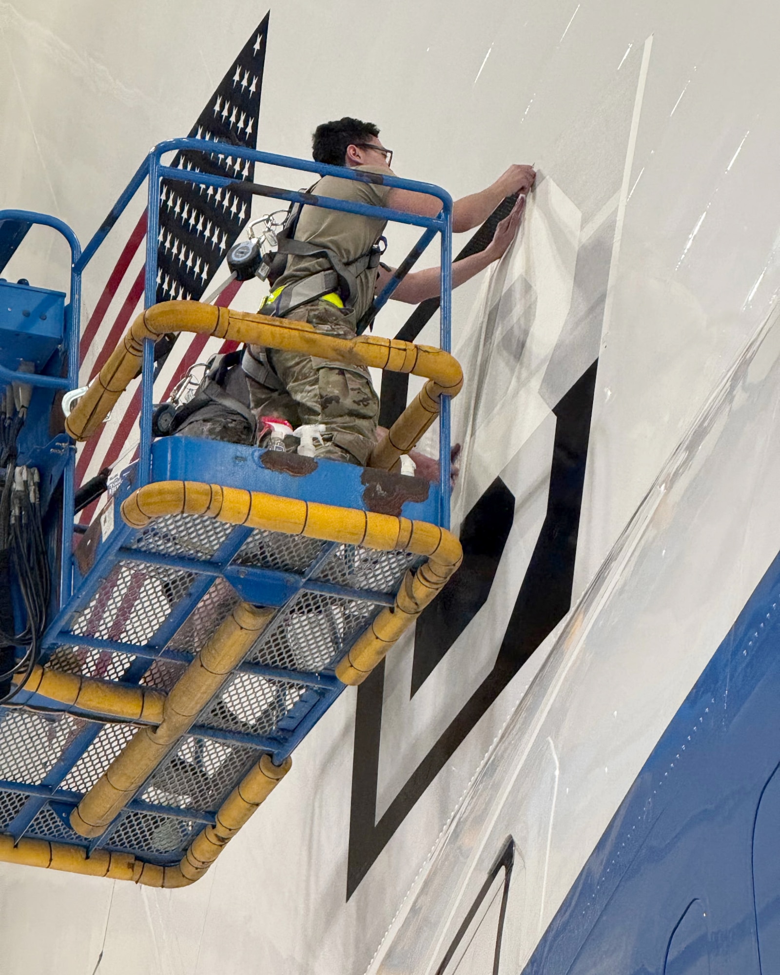 An Airman assigned to the 95th Maintenance Group removes tape from a Square B vinyl applique