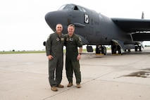 Two men stand in from of an aircraft.