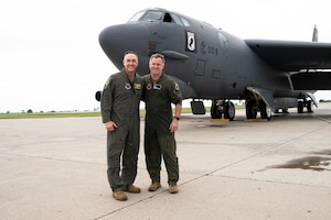 Two men stand in from of an aircraft.
