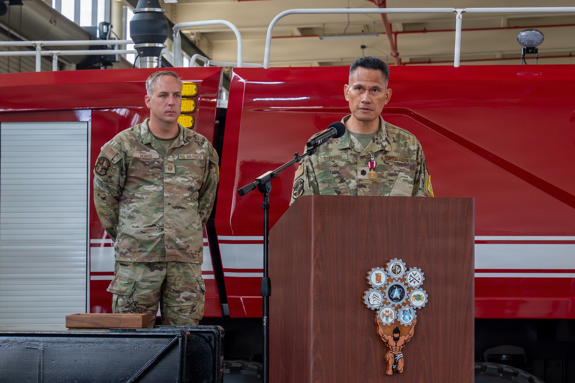 A person stands behind a podium and speaks as another person stands behind them and listens
