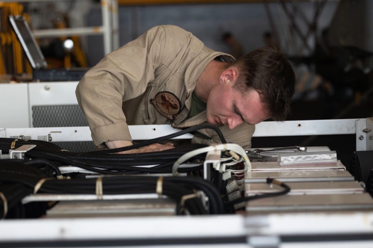 A Marine works on a piece of equipment with black cables on top of it.