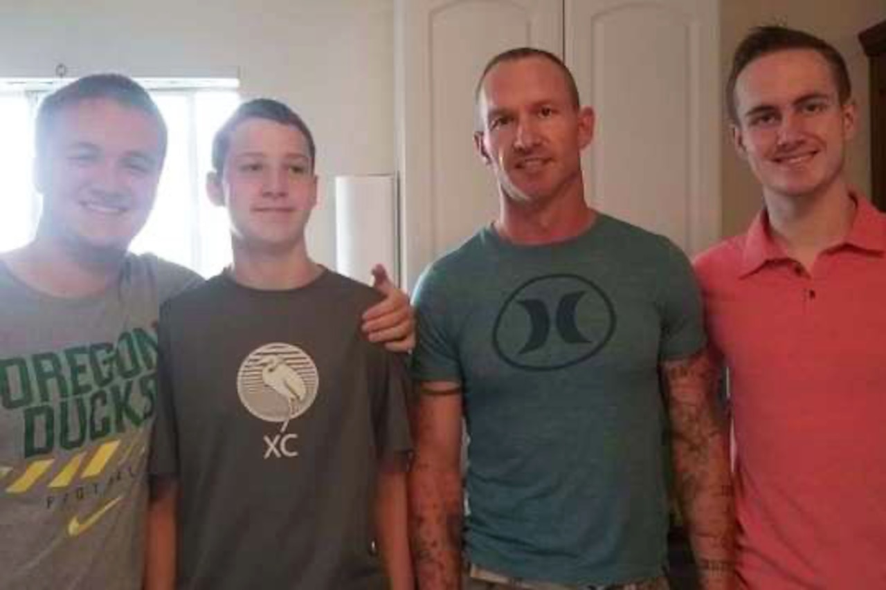 Four people in civilian attire stand in a room indoors and smile for the camera.