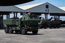 Military vehicles drive on the flightline.