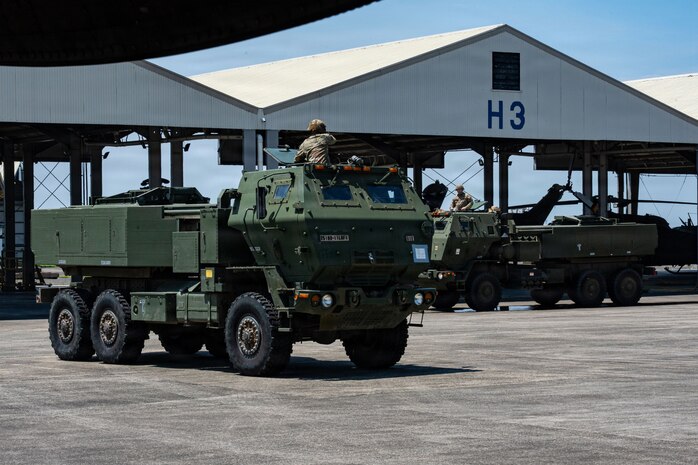 Military vehicles drive on the flightline.