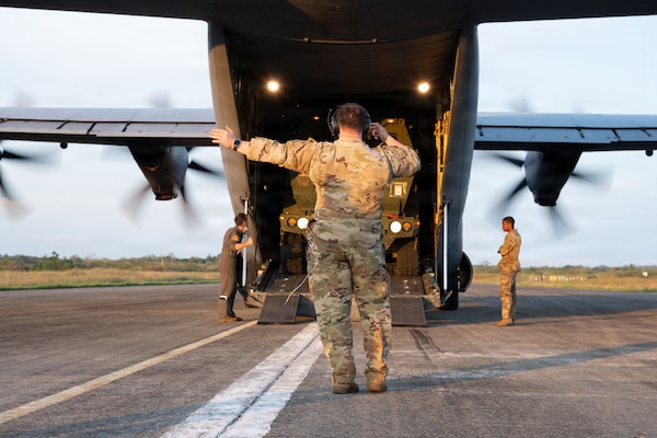 A servicemember gives hand signals behind an aircraft
