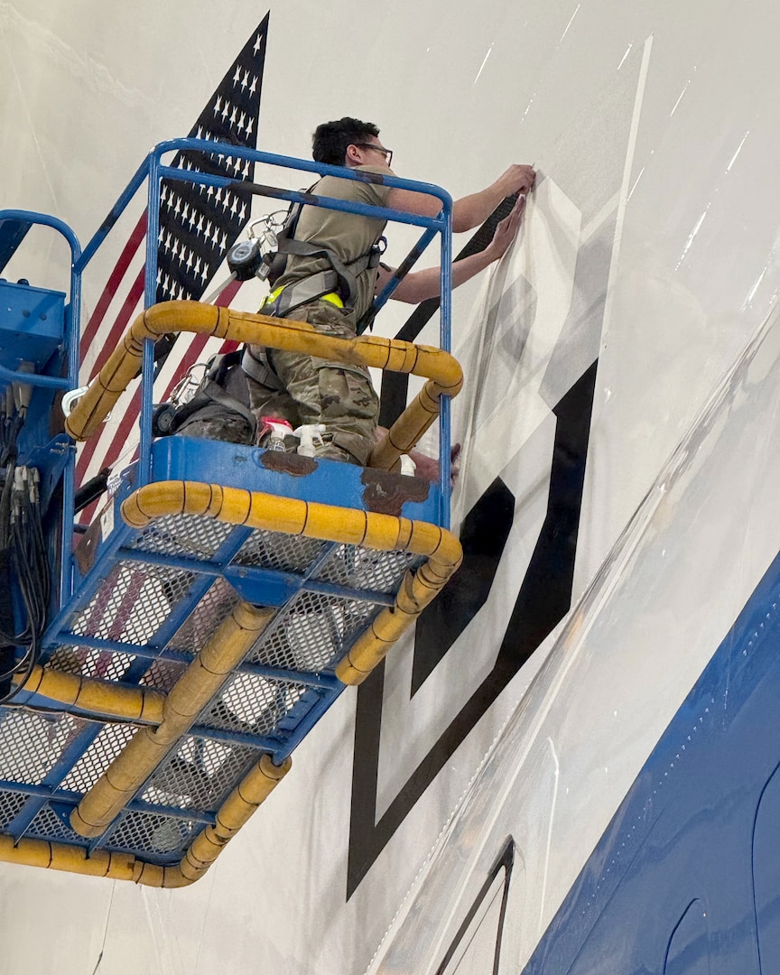 An Airman assigned to the 95th Maintenance Group removes tape from a Square B vinyl applique