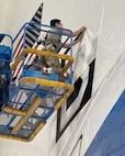 An Airman assigned to the 95th Maintenance Group removes tape from a Square B vinyl applique