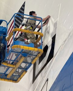 An Airman assigned to the 95th Maintenance Group removes tape from a Square B vinyl applique