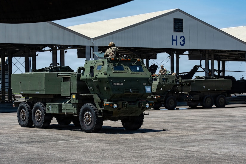 Military vehicles drive on the flightline.