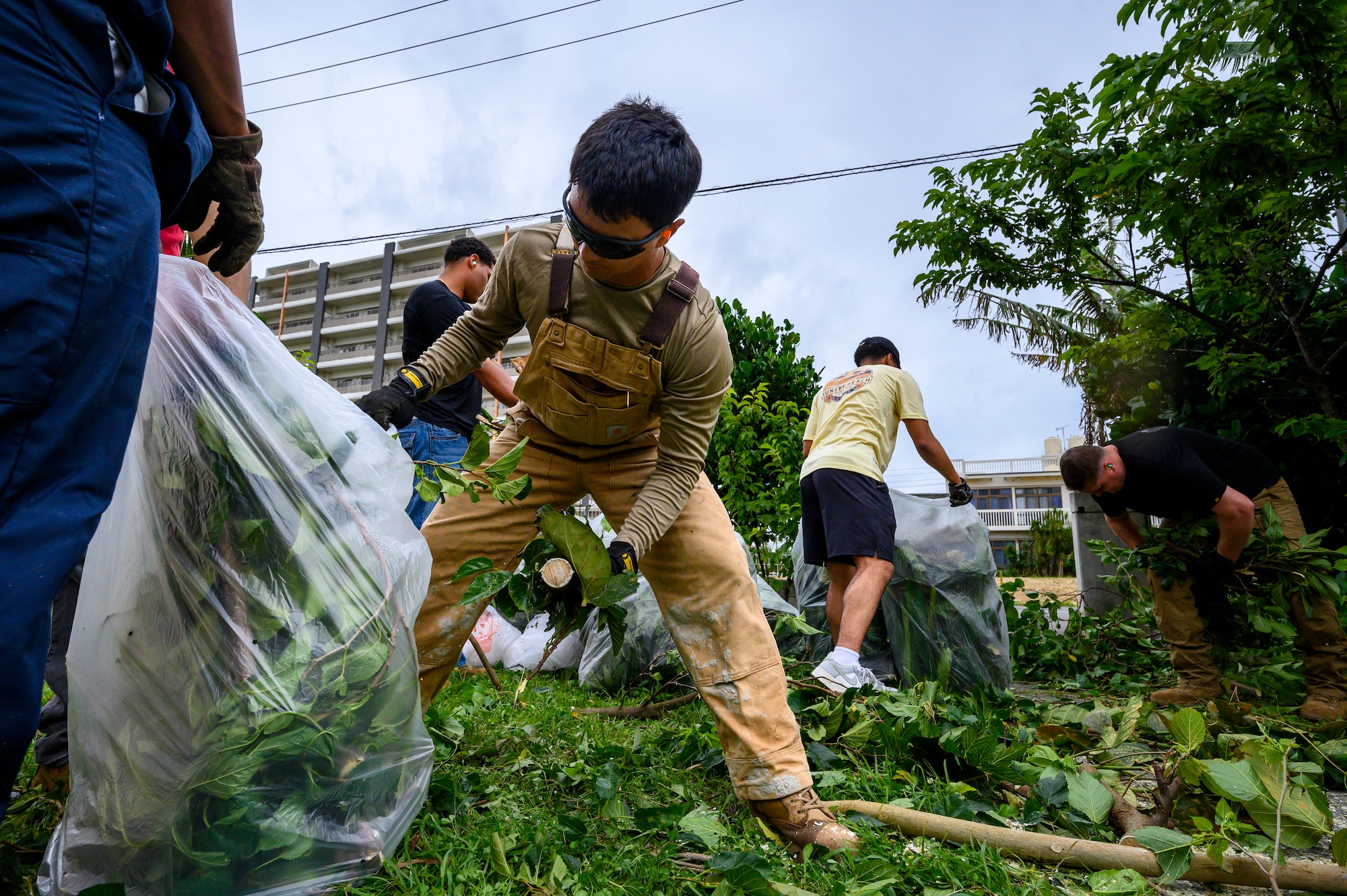 U.S. Air Force Airman Joshua Hernandez, 18th CES pavements and equipment journeyman, places vegetation into a collection bag during a volunteer cleanup project at Misato Children’s Home in Okinawa, Japan, June 12, 2026. Volunteers removed overgrown brush and storm debris to improve the safety and appearance of the facility's outdoor areas. (U.S. Air Force photo by Airman 1st Class Francisco Huerta)
