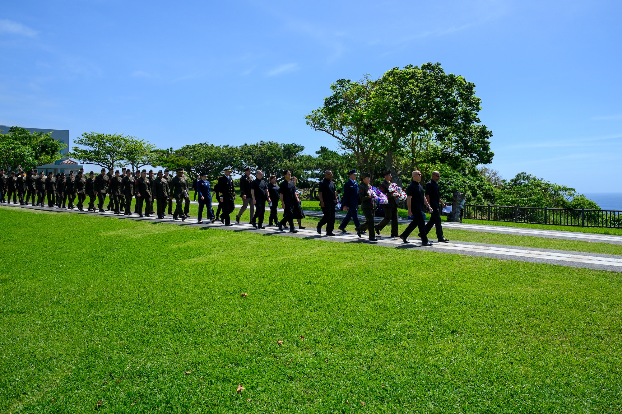 U.S. Marines assigned to III Marine Expeditionary Force carry ceremonial wreaths while members of the presenting party walk toward “The Cornerstone of Peace” during the Okinawa Memorial Day ceremony at Peace Memorial Park, Okinawa, Japan, June 23, 2026. The ceremony, hosted by the American Chamber of Commerce in Okinawa and USO Okinawa, commemorates the end of the Battle of Okinawa and honors those who sacrificed their lives during the campaign. (U.S. Air Force photo by Airman 1st Class Francisco Huerta)