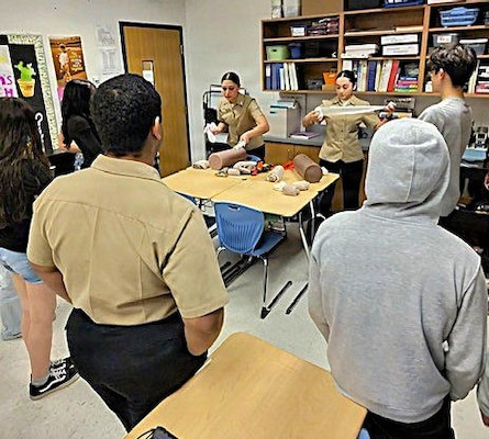 Hospitalman Apprentice Elisa Medina-Moya, left, and Hospitalman Apprentice Kaitlyn Lewis, right, both assigned to Navy Medicine Readiness and Training Command (NMRTC) Patuxent River, demonstrate Tactical Combat Casualty Care (TCCC) techniques to students at Spring Ridge Middle School. The hands-on presentation was part of the school's annual Career Day, where the Sailors showcased the life-saving skills of Navy hospital corpsmen and introduced students to career pathways in military medicine.