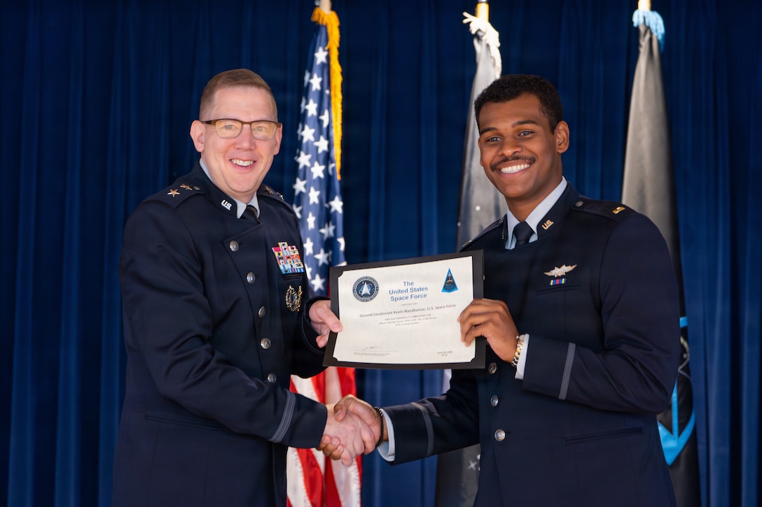 U.S. Space Force Maj. Gen. James E. Smith, commander of Space Training and Readiness Command, left, presents a certificate to a graduate during an Officer Training Course graduation ceremony at Peterson Space Force Base, Colorado, June 26, 2026.