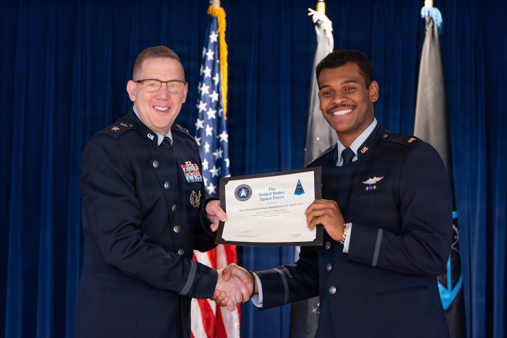 U.S. Space Force Maj. Gen. James E. Smith, commander of Space Training and Readiness Command, left, presents a certificate to a graduate during an Officer Training Course graduation ceremony at Peterson Space Force Base, Colorado, June 26, 2026.