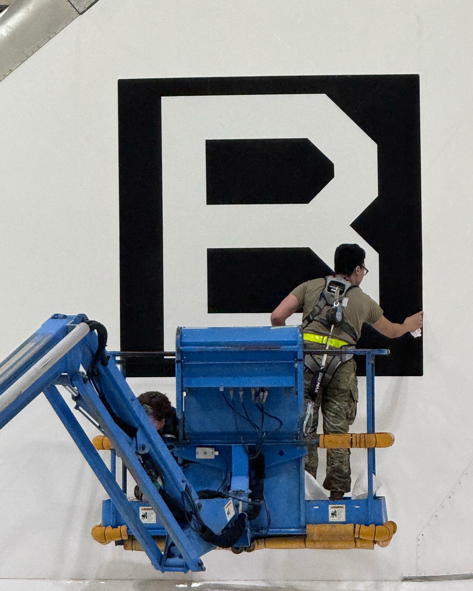 A team comprised of Airmen and civilians assigned to the 95th Maintenance Group apply an edge sealant to a Square B vinyl applique