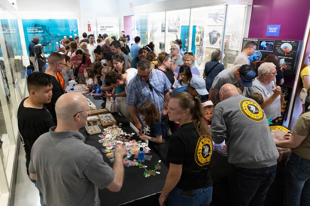Dozens of people gather in a room looking at displays about bugs.
