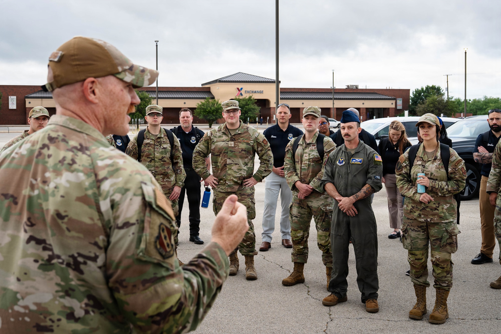 Airmen and civilians stand in a group and receive a brief