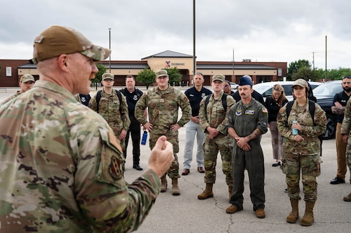 Airmen and civilians stand in a group and receive a brief