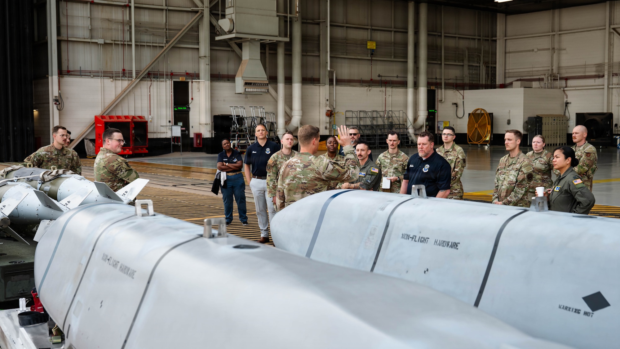 Airmen and civilians stand in a group and receive a brief